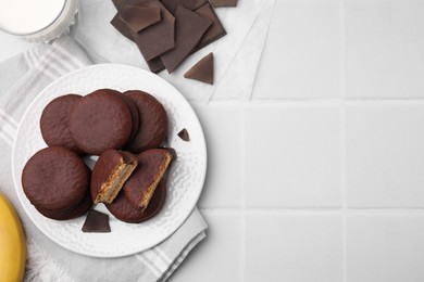 Photo of Tasty banana choco pies and pieces of chocolate on white tiled table, flat lay. Space for text