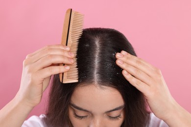 Photo of Woman with comb examining her hair and scalp on pink background, closeup. Dandruff problem