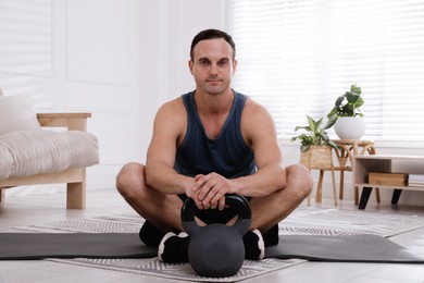 Photo of Muscular man sitting with kettlebell on mat at home
