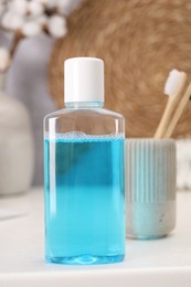 Photo of Bottle of mouthwash and toothbrushes on white table in bathroom