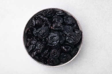 Sweet dried prunes in bowl on light table, top view