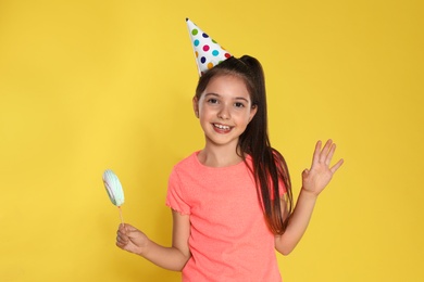 Happy girl with candy on yellow background. Birthday celebration