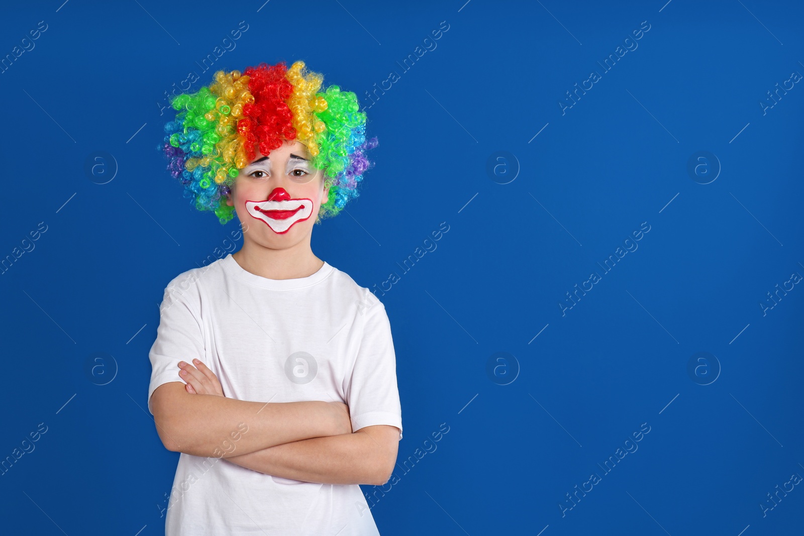 Photo of Preteen boy with clown makeup and wig on blue background, space for text. April fool's day