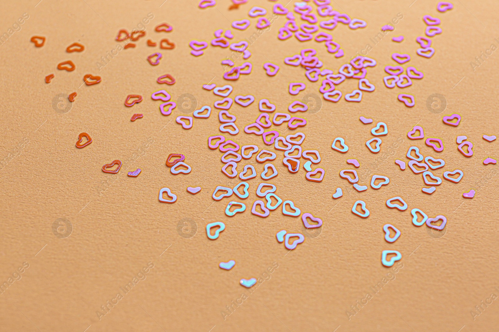 Photo of Shiny bright heart shaped glitter on beige background