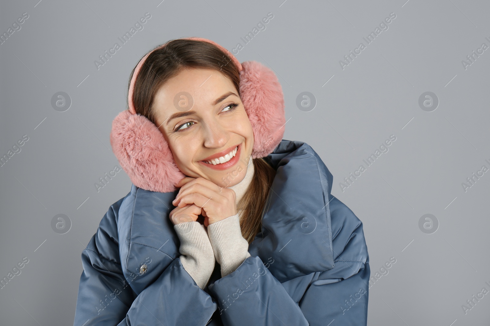 Photo of Happy woman wearing warm earmuffs on grey background