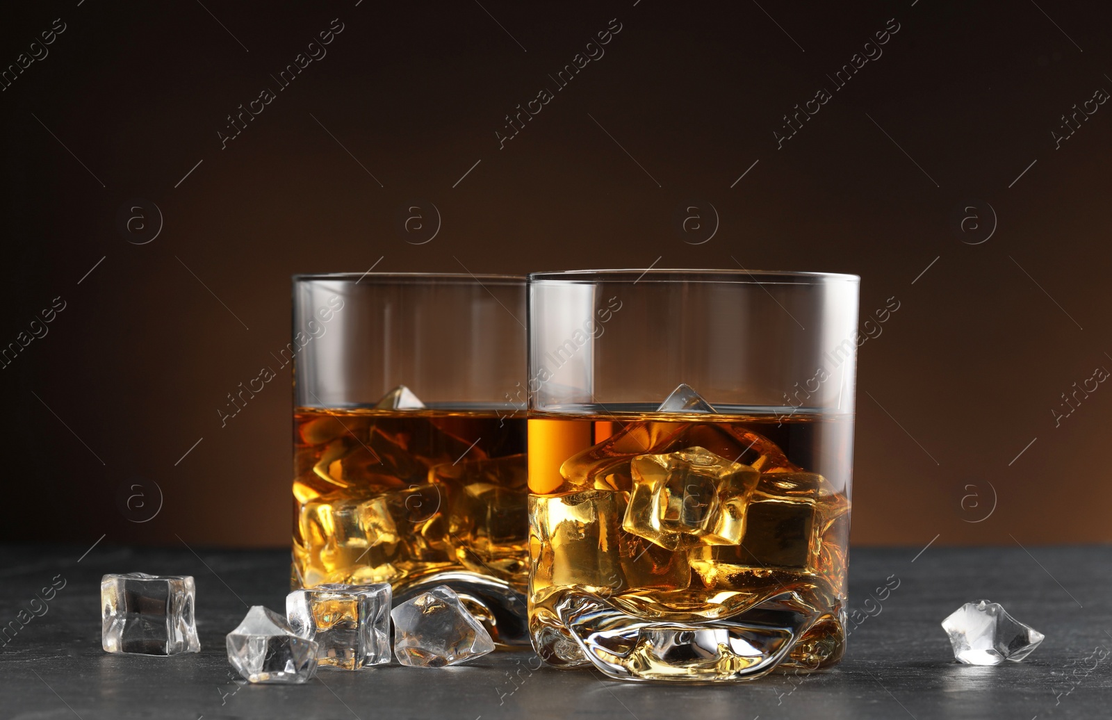 Photo of Whiskey and ice cubes in glasses on black table, closeup