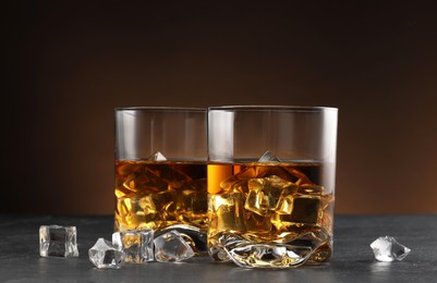 Whiskey and ice cubes in glasses on black table, closeup