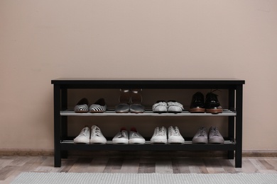 Shoe rack with different footwear near color wall. Stylish hallway interior