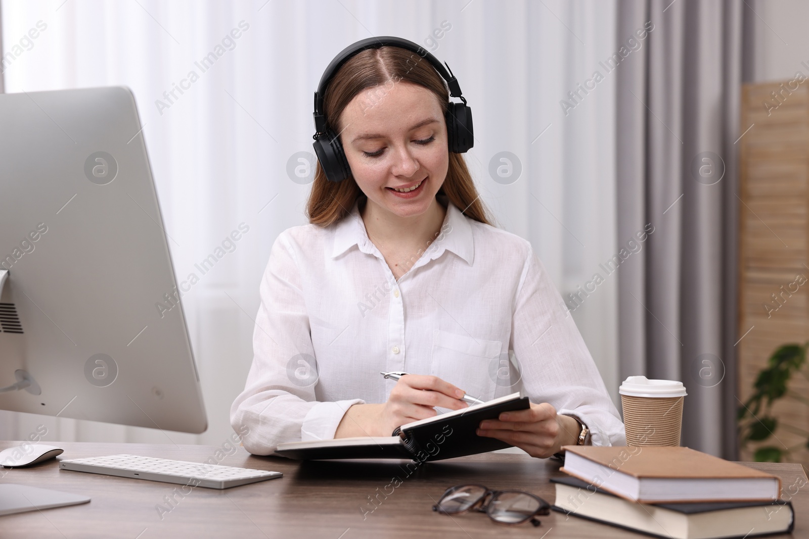 Photo of E-learning. Young woman taking notes during online lesson at wooden table indoors