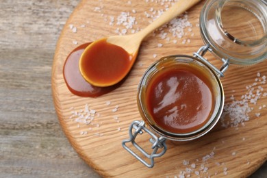 Photo of Jar and spoon with tasty salted caramel on wooden table, top view