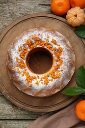 Photo of Homemade yogurt cake with tangerines, powdered sugar and green leaves on wooden table, flat lay