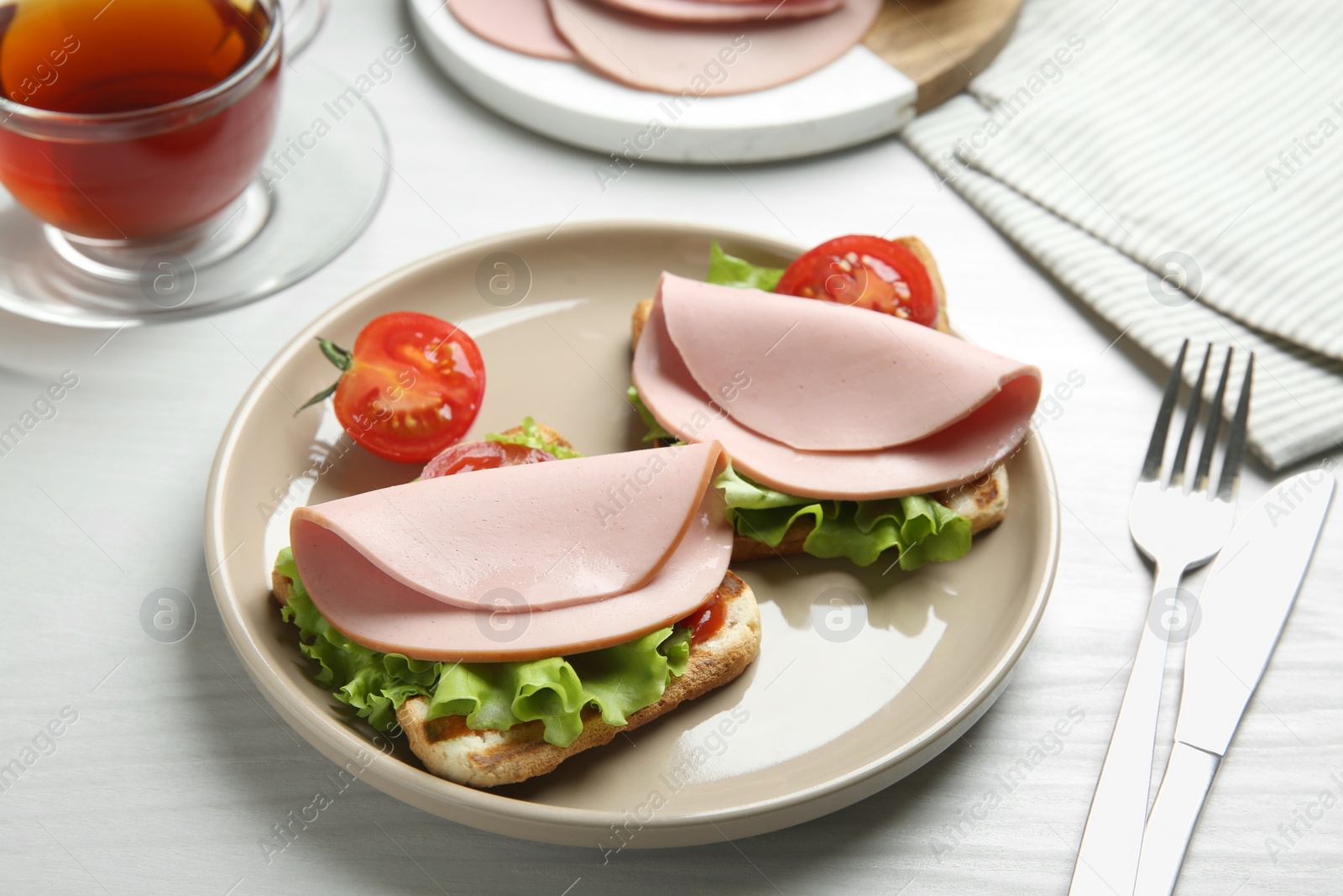 Photo of Plate of tasty sandwiches with boiled sausage, tomato and lettuce on white wooden table