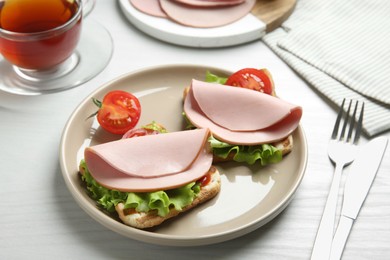 Photo of Plate of tasty sandwiches with boiled sausage, tomato and lettuce on white wooden table