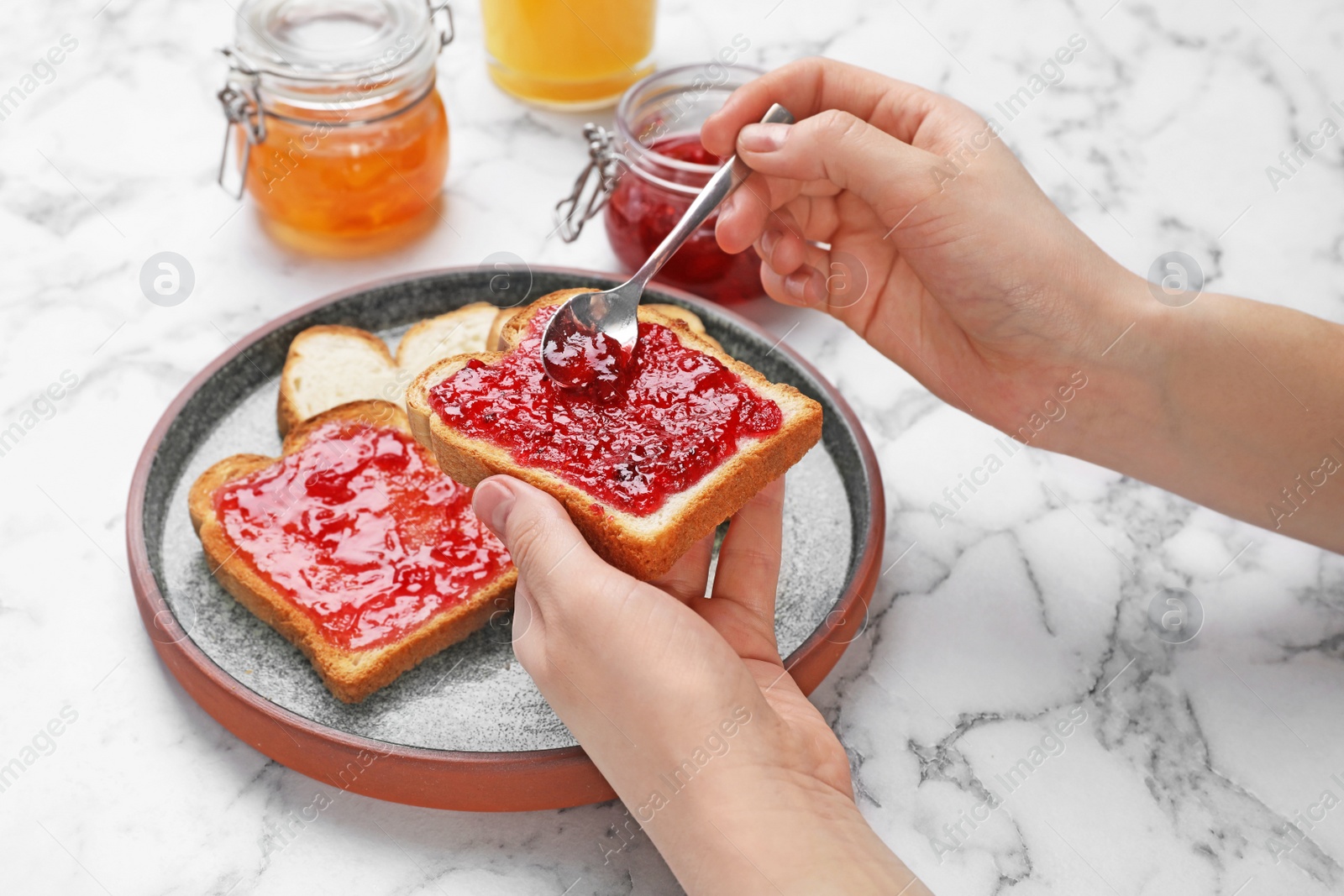 Photo of Woman spreading jam on toast over table