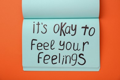 Photo of Notebook with phrase It`s Okay To Feel Your Feelings on orange background, top view