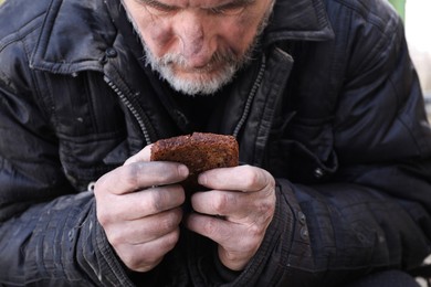 Photo of Poor homeless man holding piece of bread outdoors
