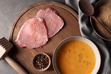 Photo of Cooking schnitzel. Raw pork slices, other ingredients and meat tenderizer on grey textured table, flat lay