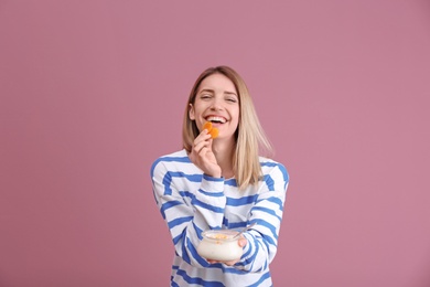 Young attractive woman eating tasty yogurt on color background