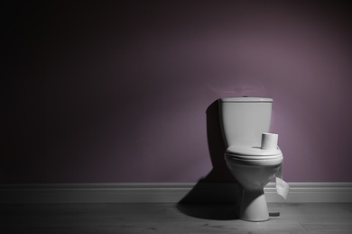 Photo of New ceramic toilet bowl and roll of toilet paper near color wall with space for text
