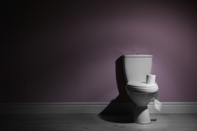 New ceramic toilet bowl and roll of toilet paper near color wall with space for text