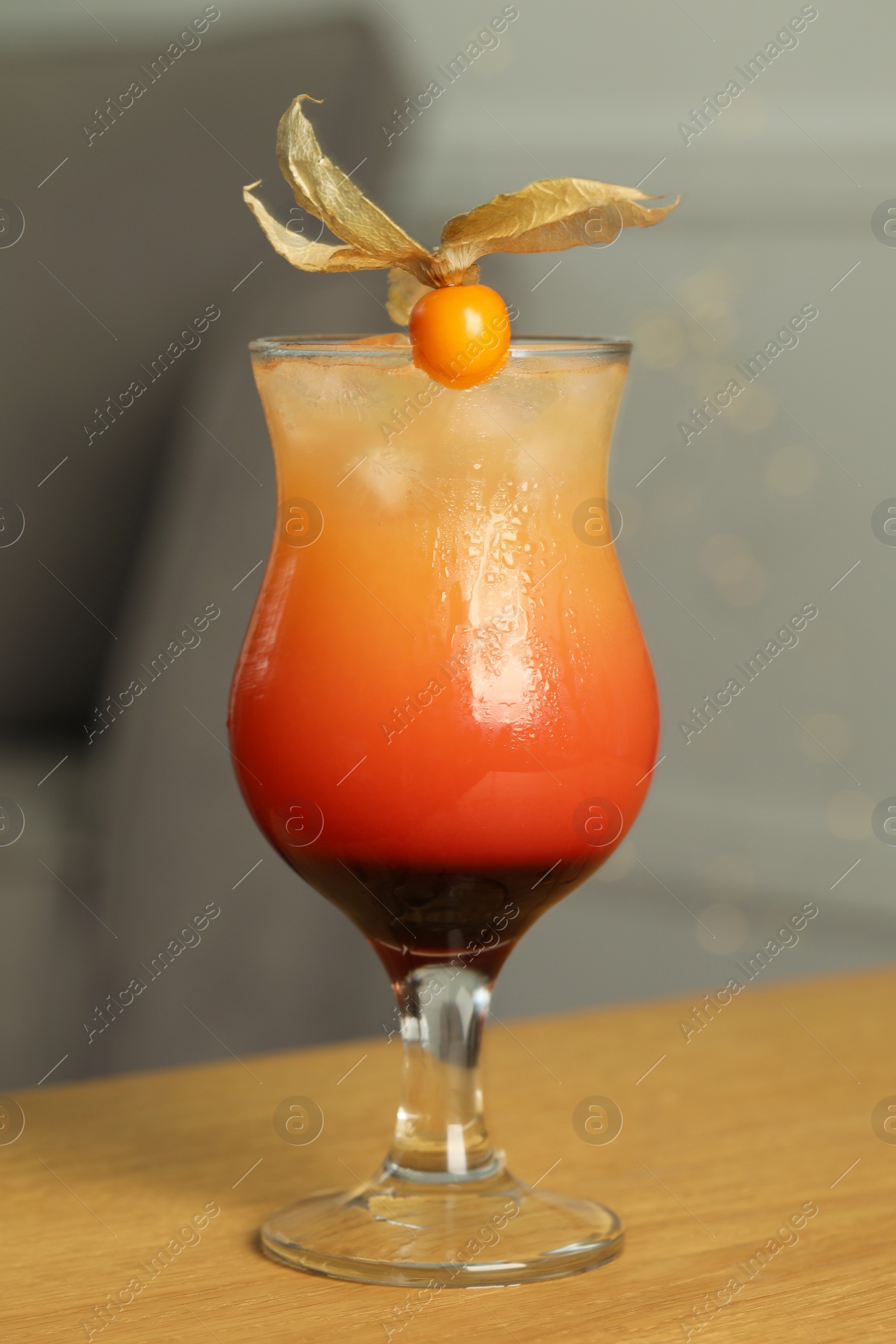 Photo of Refreshing cocktail decorated with physalis fruit on wooden table indoors