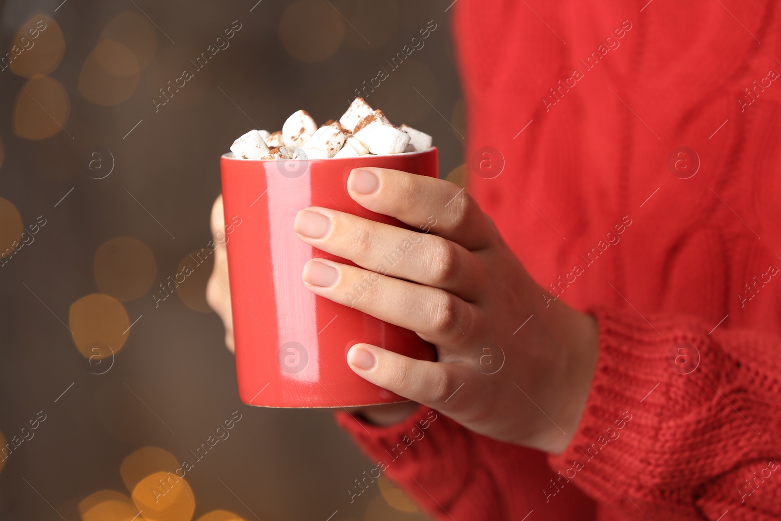 Photo of Woman holding cup of tasty cocoa with marshmallows on blurred background