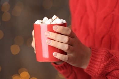 Woman holding cup of tasty cocoa with marshmallows on blurred background