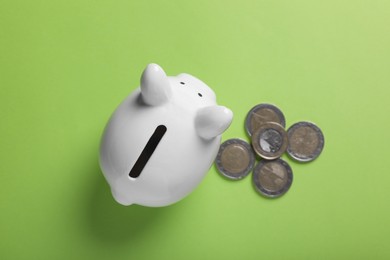 Ceramic piggy bank and coins on light green background, flat lay. Financial savings