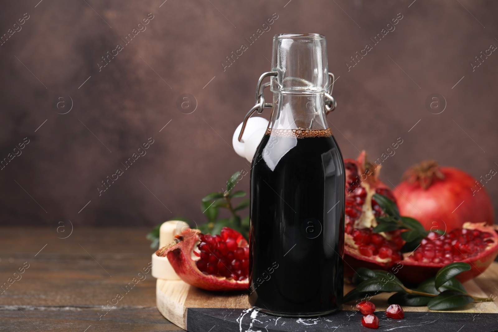 Photo of Tasty pomegranate sauce in bottle, fruits and branches on wooden table, closeup. Space for text