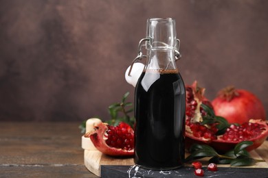 Tasty pomegranate sauce in bottle, fruits and branches on wooden table, closeup. Space for text