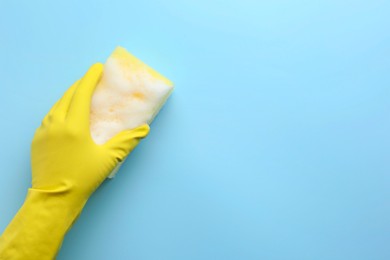 Cleaner in rubber glove holding sponge with foam on light blue background, top view. Space for text