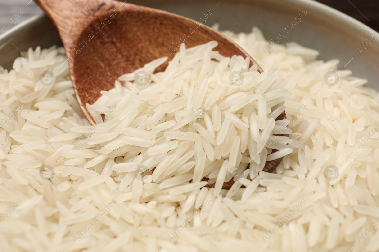 Photo of Raw basmati rice and wooden spoon in bowl on table, closeup