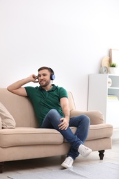 Photo of Young man in headphones enjoying music on sofa at home