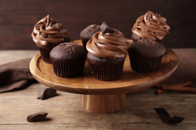 Photo of Delicious chocolate muffins and cupcakes decorated with cream on wooden table