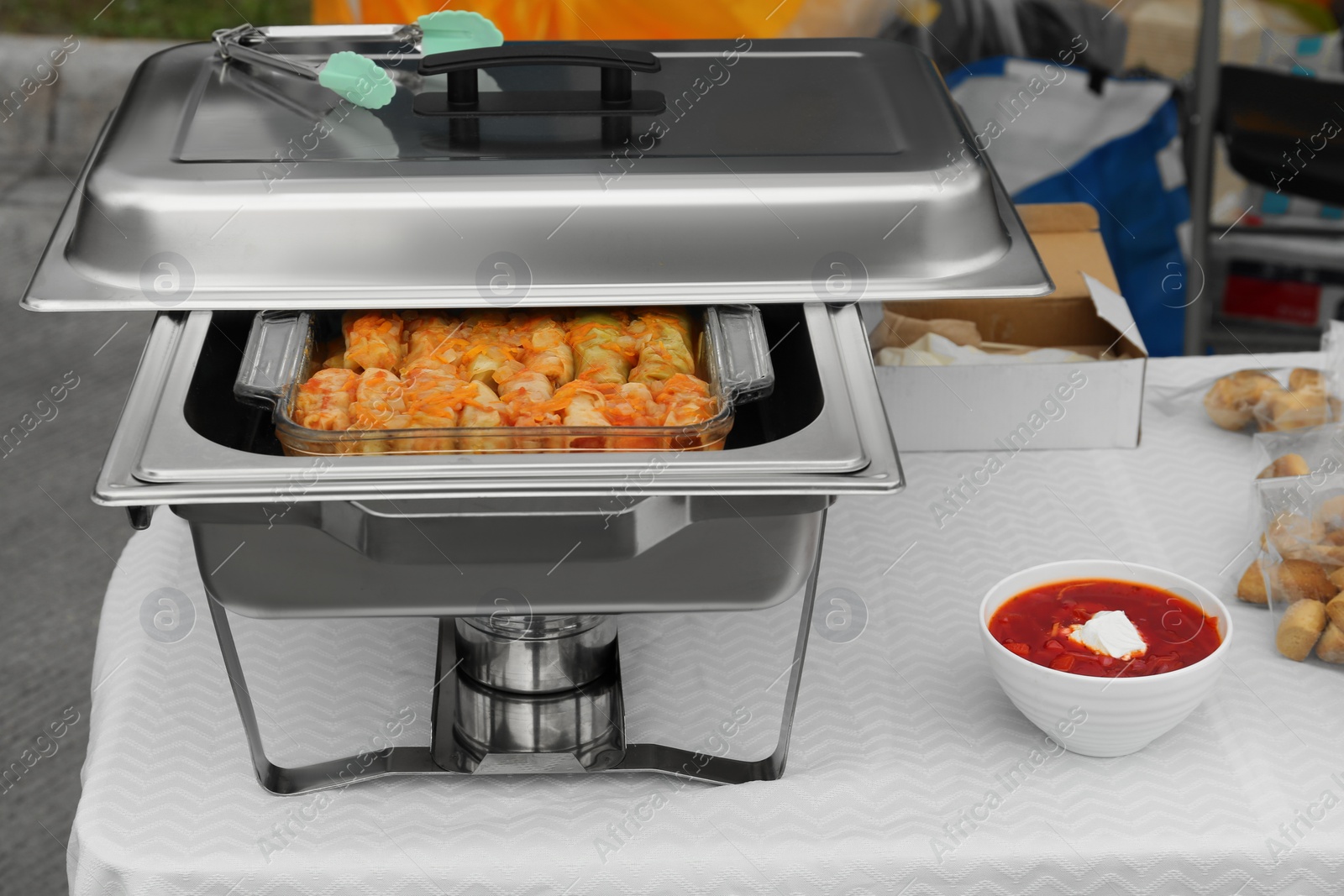 Photo of Volunteer food distribution. Metal warmer with tasty stuffed cabbage and bowl of borsch served on table outdoors