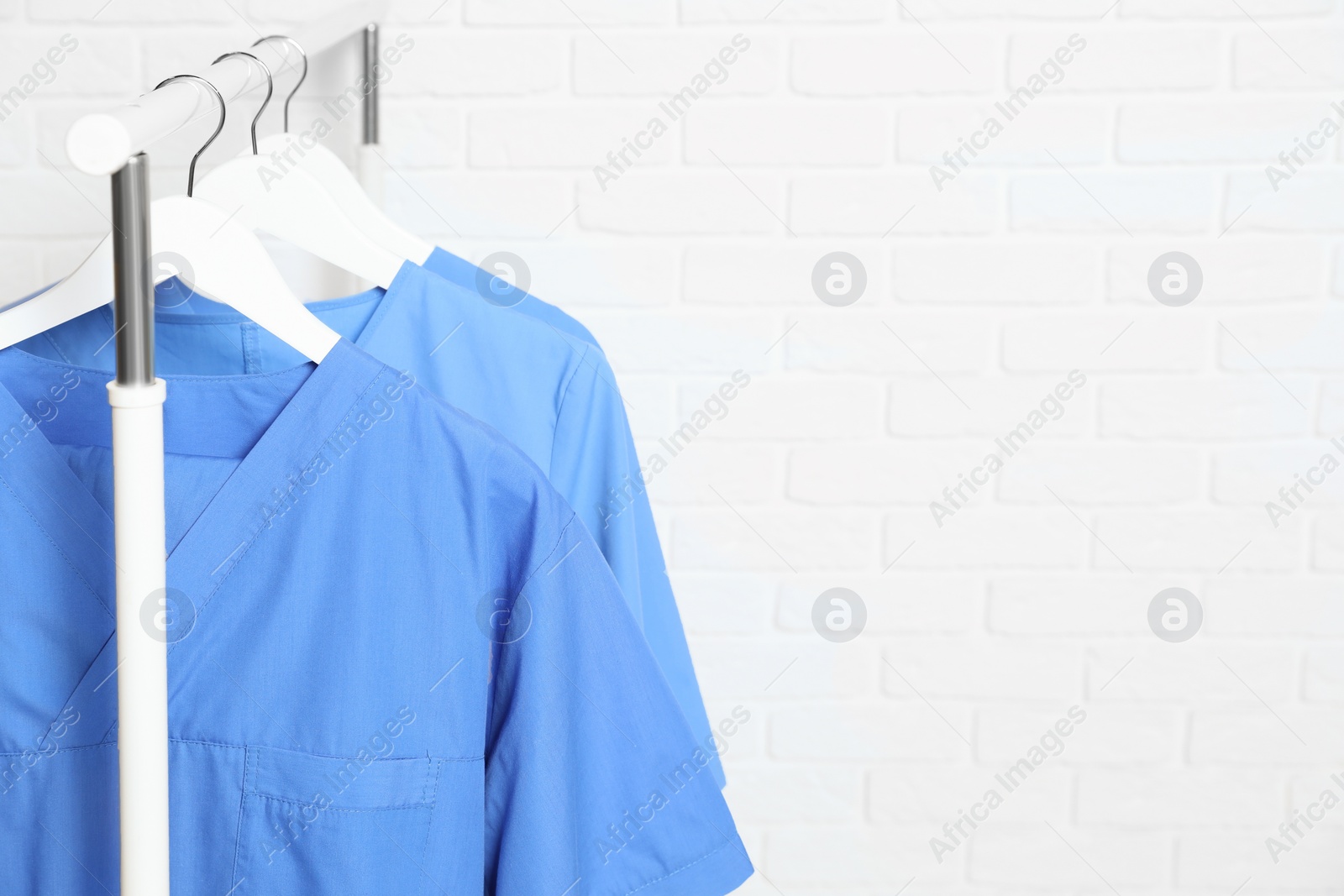 Photo of Medical uniforms hanging on rack near white brick wall. Space for text