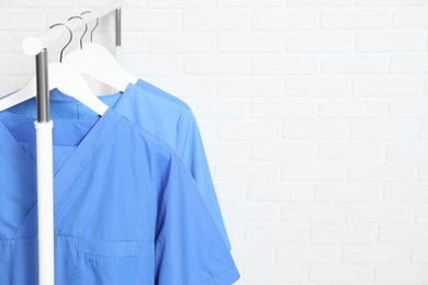 Photo of Medical uniforms hanging on rack near white brick wall. Space for text