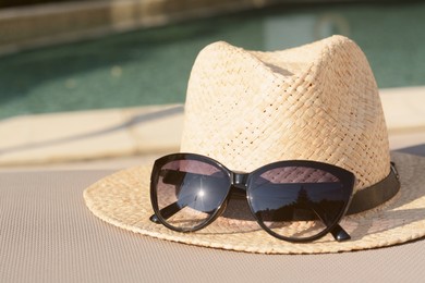 Stylish hat and sunglasses near outdoor swimming pool, closeup. Space for text