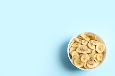 Bowl with banana slices on color background, top view with space for text. Dried fruit as healthy snack