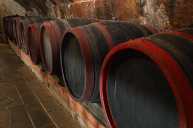 Photo of Many wooden barrels with alcohol drinks in cellar