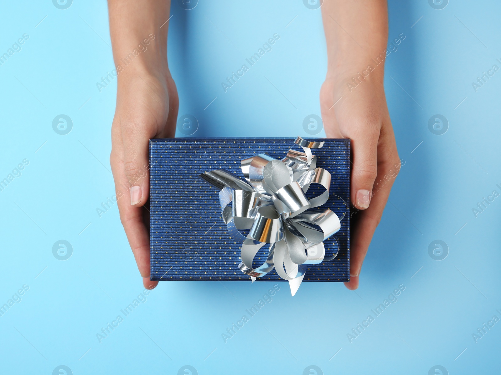 Photo of Woman holding beautiful gift box on blue background, top view