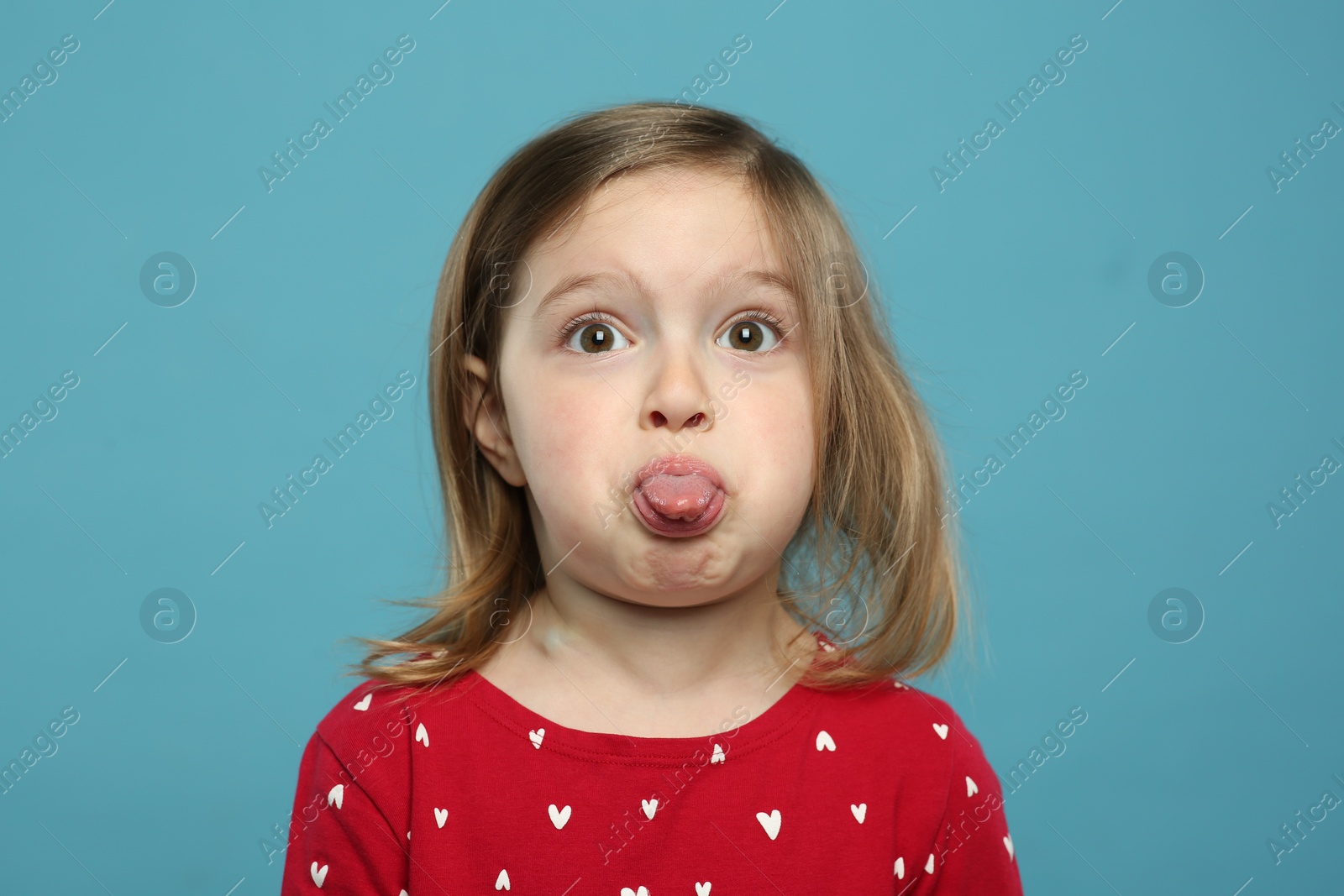 Photo of Funny little girl showing her tongue on light blue background