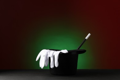 Photo of Magician's hat, wand and gloves on black wooden table against dark background, space for text