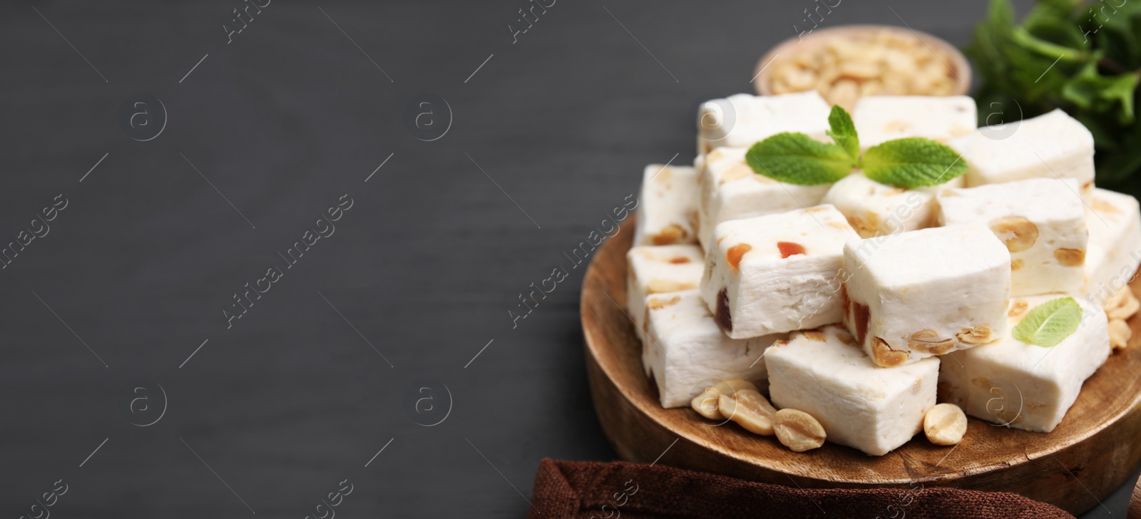 Image of Pieces of delicious nutty nougat on gray wooden table, space for text. Banner design