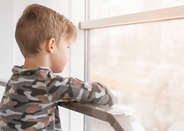 Photo of Lonely little boy near window indoors. Child autism