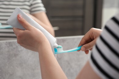 Woman squeezing toothpaste from tube onto toothbrush near mirror in bathroom, closeup