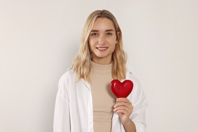 Happy volunteer holding red heart with hands on light background