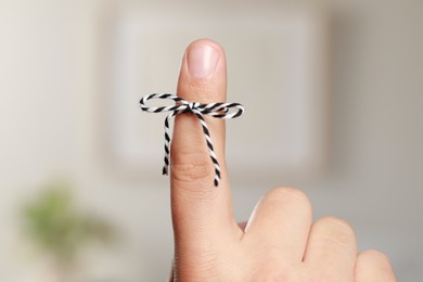 Photo of Man showing index finger with tied bow as reminder on blurred background, closeup