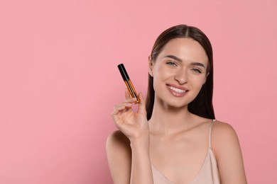 Young woman with eyelash oil on pink background, space for text