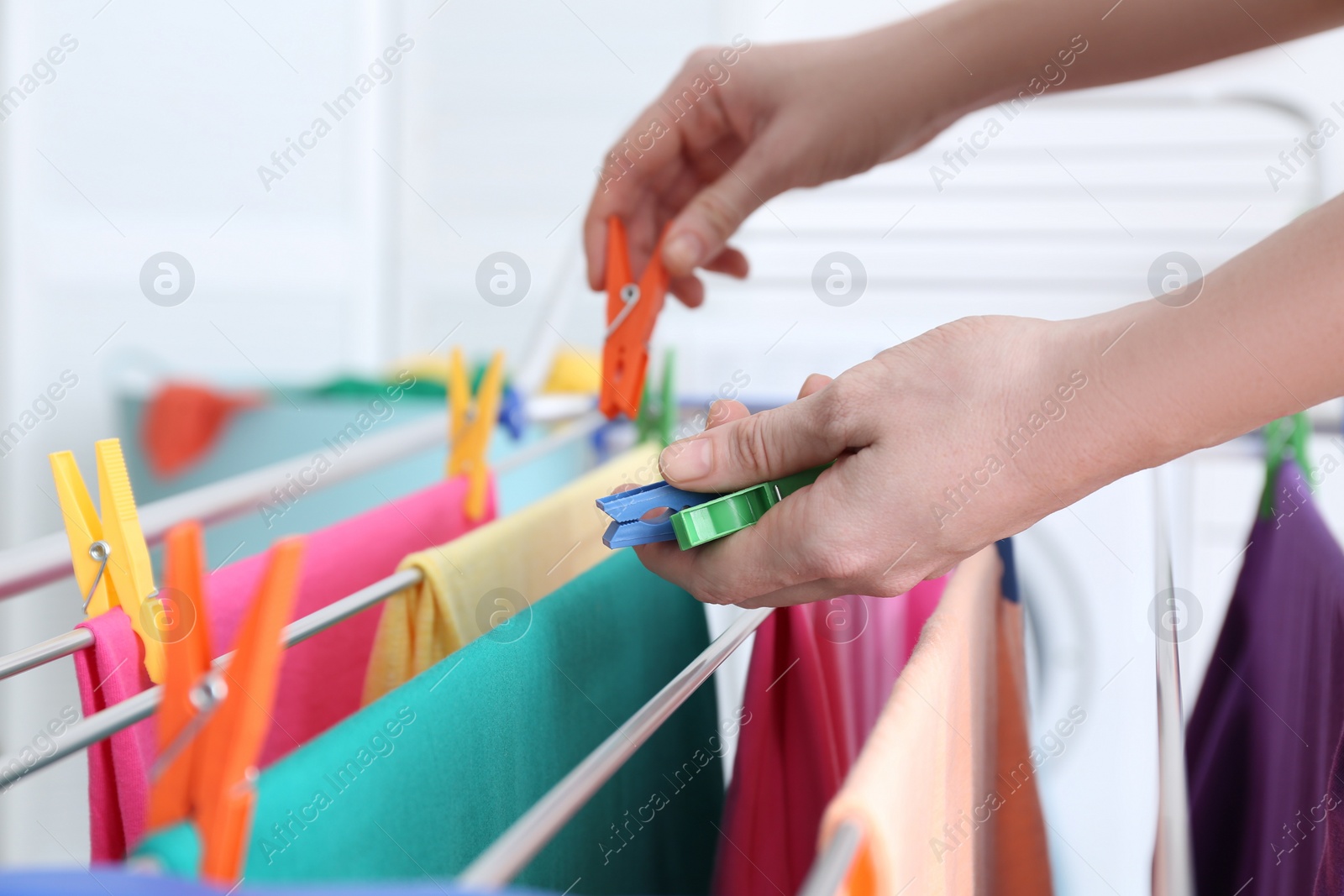 Photo of Woman hanging clean laundry on drying rack indoors, closeup